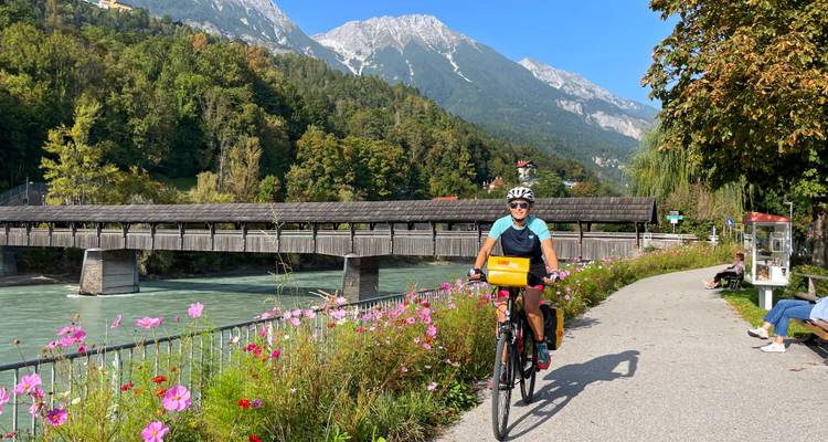 Ein Radfahrer auf einem Weg neben einem Fluss und einer Holzbrücke.