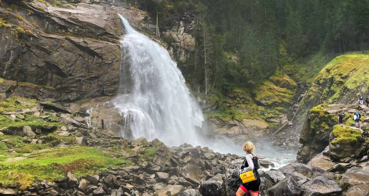 Eine Frau, die einen Wasserfall in einem bewaldeten Gebiet beobachtet.