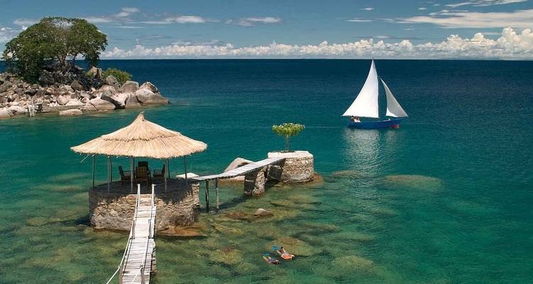 A scenic view of a lake with a stone hut and a sailboat.