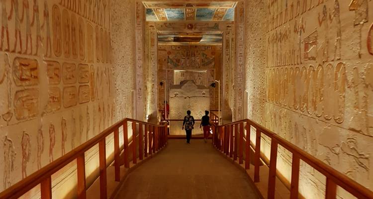 Toeristen die door een versierde gang van een oud graf lopen met ingewikkelde muursculpturen.