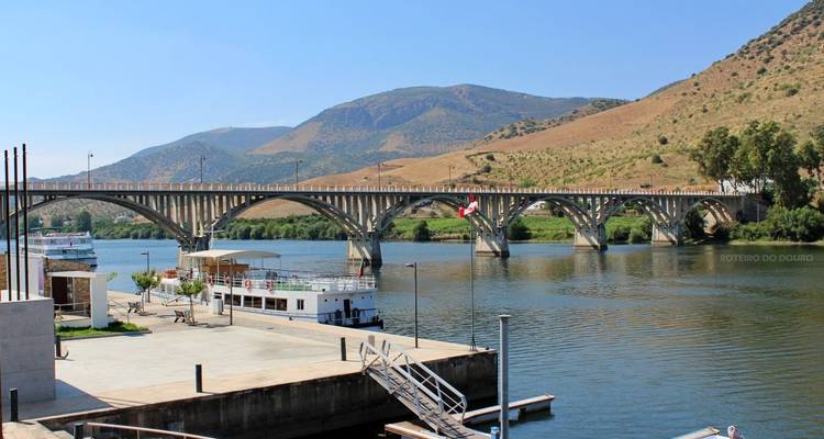 Steinbrücke über einem ruhigen Fluss vor einer Bergkulisse.