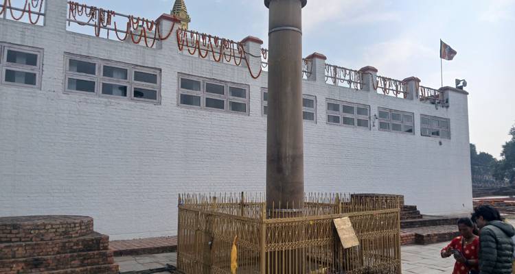 Sacred site with an Ashoka pillar and visitors.