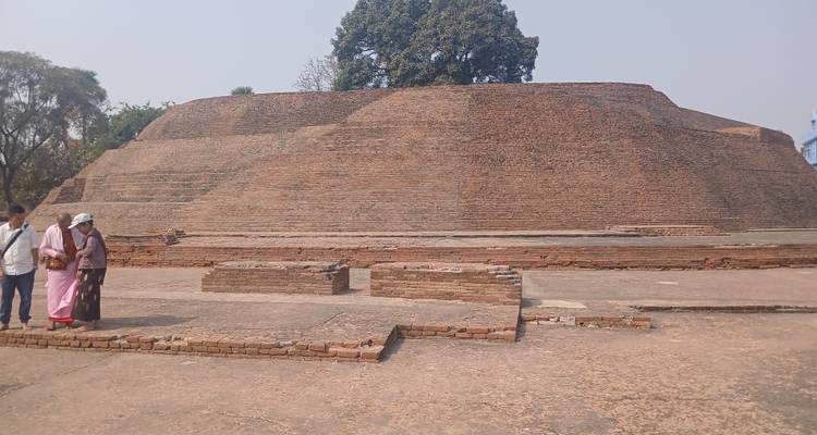 Three people walking by a large ancient brick structure.