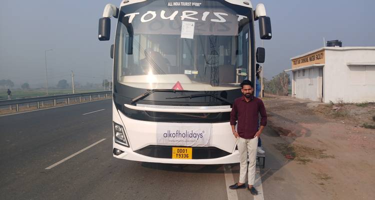 Man posing in front of a tourist bus on a highway.
