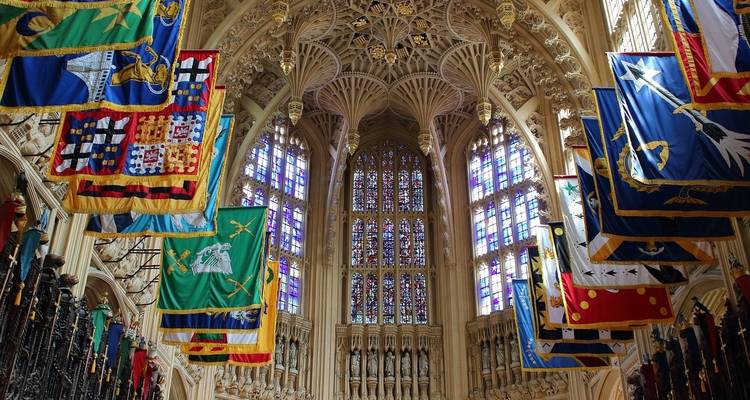 Interior of a grand chapel adorned with colorful banners and stained glass windows.