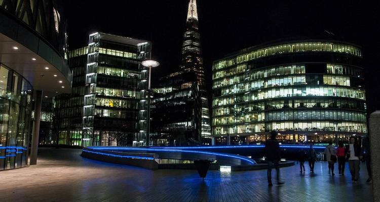 Modern cityscape at night with illuminated buildings and people walking.