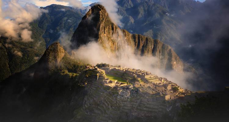 Ikonische Luftaufnahme von Machu Picchu, umhüllt von Nebel, mit dramatischen Bergen im Hintergrund.