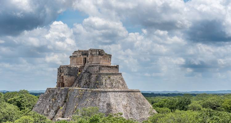 Oval-shaped pyramid surrounded by lush greenery under a blue sky.