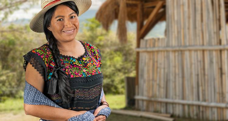 Portrait of a smiling woman in colorful traditional clothing and hat standing outdoors.