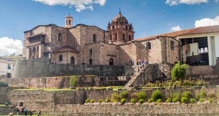Historisch stenen kerk- en kloostercomplex in Cusco gelegen op hoge muren met bezoekers eronder.