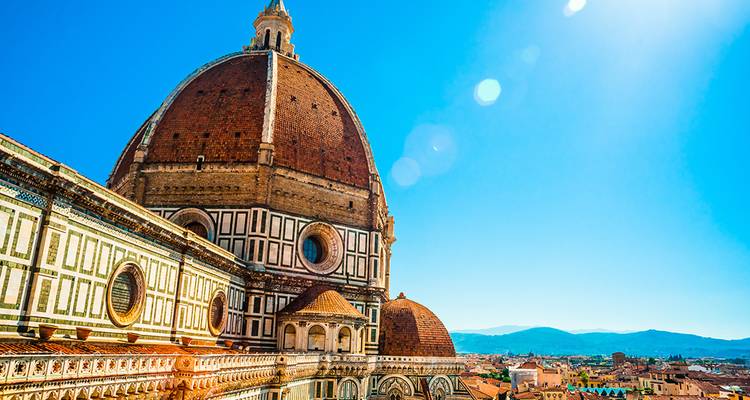 La brillante luz del sol ilumina la cúpula de terracota y el exterior de mármol ornamentado del icónico Duomo de Florencia contra un cielo azul.