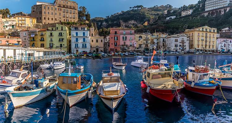 Coloridos barcos pesqueros se mecen en el vibrante puerto rodeado de edificios en tonos pastel y colinas exuberantes en Sorrento.