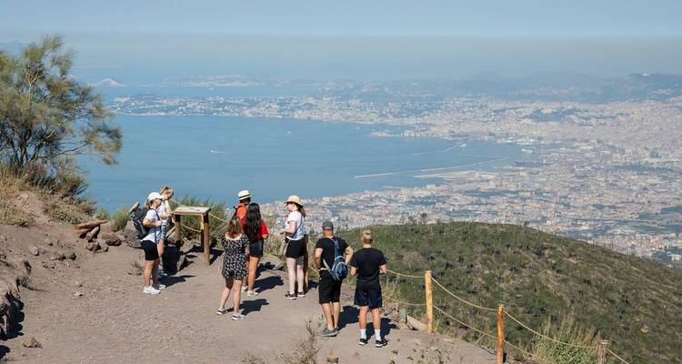Los viajeros se detienen en un mirador vallado en el Monte Vesubio con vistas panorámicas de la Bahía de Nápoles abajo.