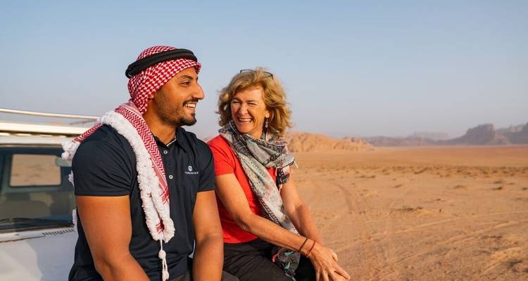 Zwei Personen sitzen auf einem Fahrzeug in einer Wüstenumgebung.