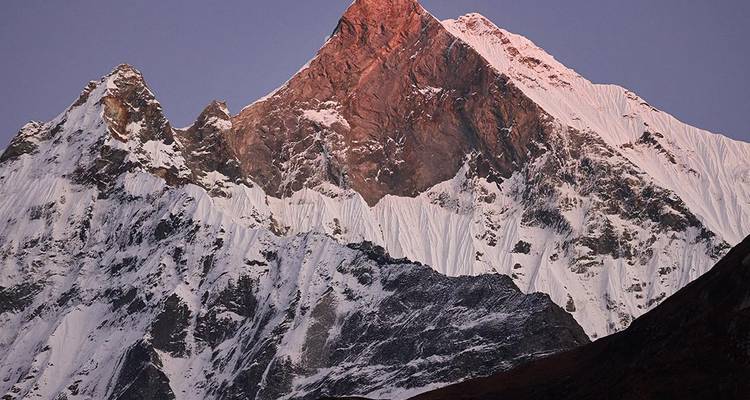 Besneeuwde Himalaya-top die roze gloeit in het vroege ochtendlicht tegen een heldere hemel.