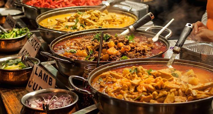 Kleurrijke reeks van dampende curry's en ingrediënten uitgestald bij een drukke eetstalletje.