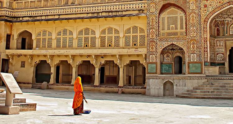 Vrouw in felloranje sari staat in een sierlijke binnenplaats van Amber Fort in Rajasthan.