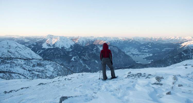 Personne debout dans la neige contemplant un paysage de montagne hivernal.