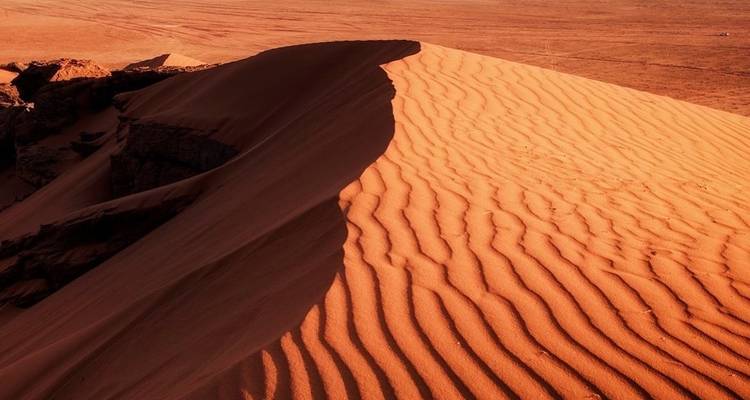 Sanddüne mit tiefen Schattenmustern in einer Wüstenlandschaft.