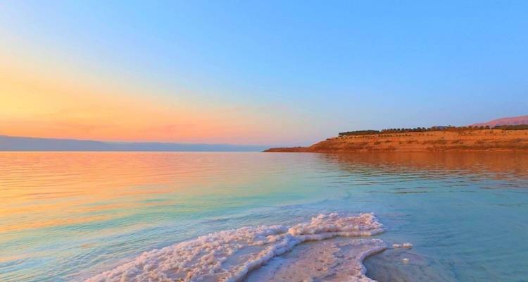 Ruhige Gewässer eines Meeres mit einer salzumrandeten Küstenlinie bei Sonnenuntergang.