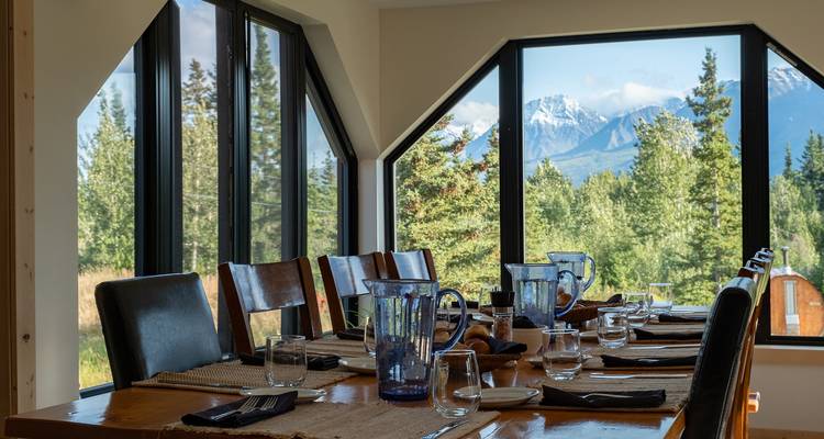 Salle à manger avec de grandes fenêtres donnant sur la forêt et les montagnes.