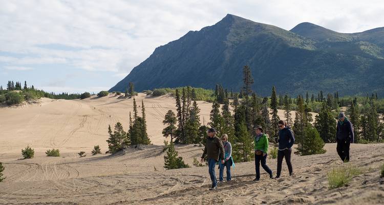 Groupe de personnes faisant de la randonnée sur des dunes avec des montagnes en arrière-plan.