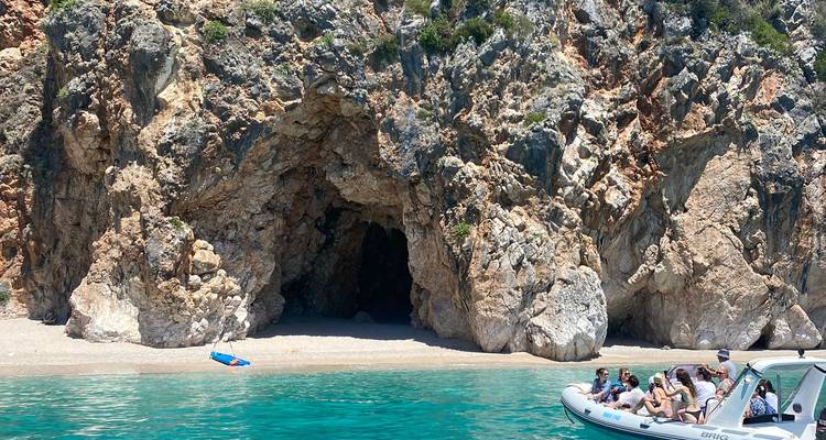 Tourists in a boat near a rocky cove with clear water.