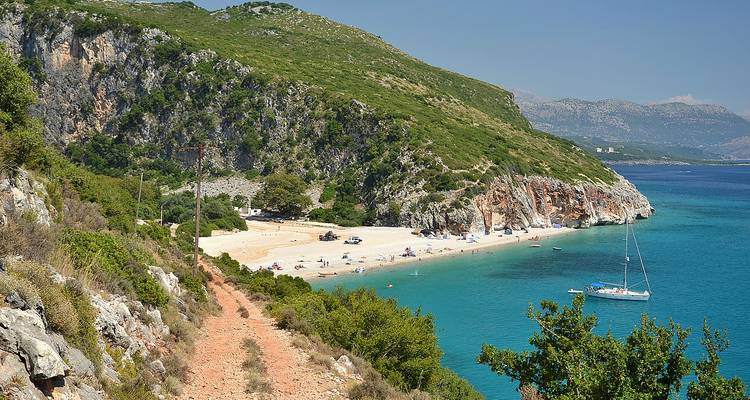 Secluded beach with a sailboat and mountainous background.