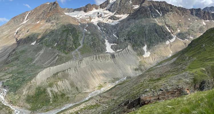 Vallée glaciaire escarpée avec des falaises striées, des crêtes rocheuses et des champs de neige estivale persistants.