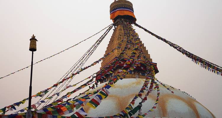 Eine Stupa mit bunten Gebetsfahnen unter einem bewölkten Himmel.
