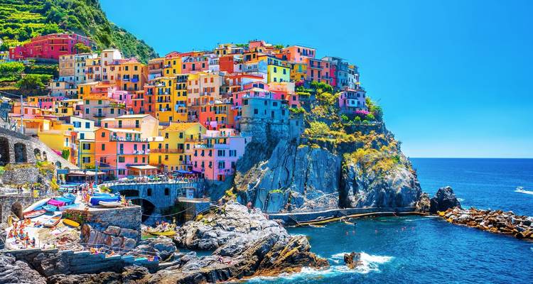 Las vibrantes casas de colores pastel de Manarola se extienden en cascada por los acantilados rocosos hacia el mar azul profundo bajo el sol brillante.
