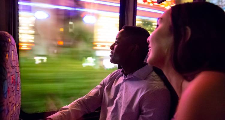 Una pareja viaja en autobús por la noche viendo cómo las luces de neón pasan rápidamente por la ventana.