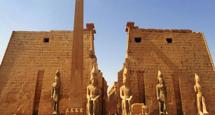 Vue diurne de l'entrée du temple de Louxor avec un obélisque imposant et des statues colossales sous un ciel bleu dégagé