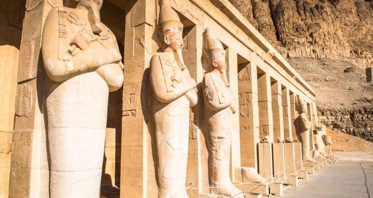 Rangée de statues colossales debout au Temple d'Hatshepsout baignées dans la lumière du soleil éclatant sur fond de falaise