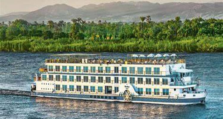 Grand navire de croisière multi-étages naviguant le long d'une large section du Nil avec des berges vertes en arrière-plan