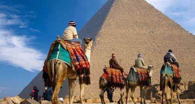 Les voyageurs montant des chameaux drapés dans des couvertures colorées avec une massive pyramide s'élevant derrière eux