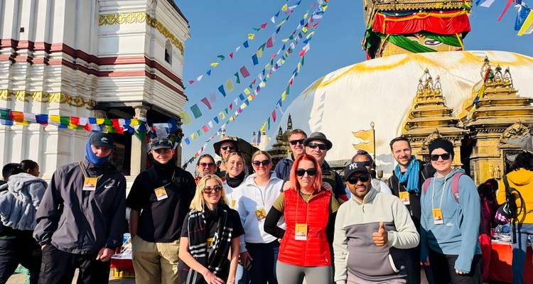 Groupe de personnes debout devant un grand stupa avec des drapeaux de prière.