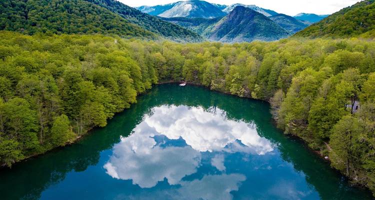 Ein ruhiger See, umgeben von dichtem Wald und Bergen.