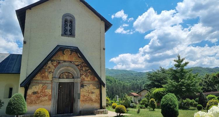 Malerischer Blick auf eine Kirche mit Bergen und lebendigen Gärten im Hintergrund.