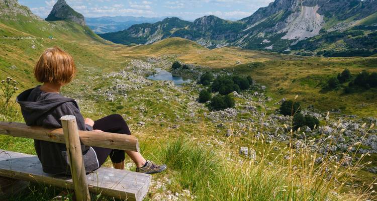 Eine Person, die auf einer Holzbank sitzt und auf ein malerisches Tal blickt.