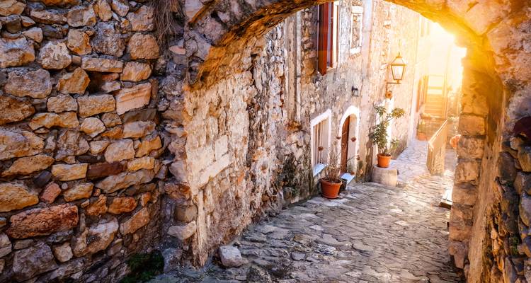 Eine schmale Steingasse in einer mittelalterlichen Stadt mit durchscheinendem Sonnenlicht.
