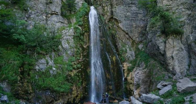Cascada en una zona rocosa boscosa con persona abajo.