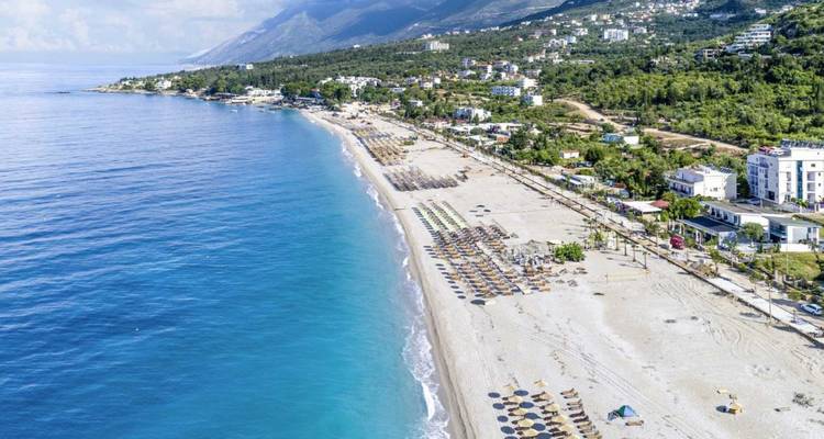 Playa en Himara con hamacas y vista lejana de montañas.