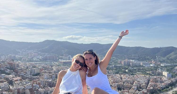 Zwei Frauen lächeln auf einem Dach mit Stadtblick.