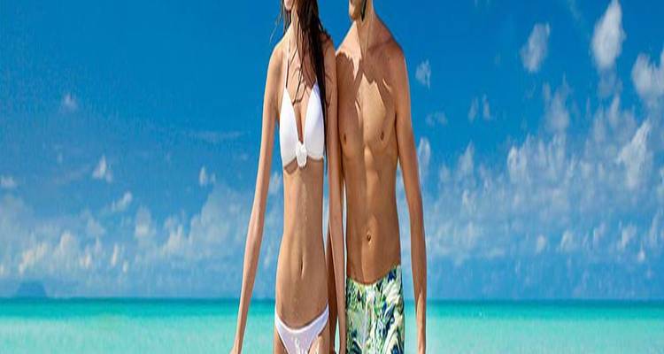 Wide panoramic crop of fit couple walking along shallow turquoise sea under bright blue sky.