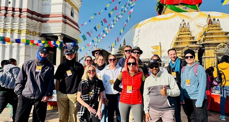 Grupo de turistas en una estupa, con nubes y banderas de oración.
