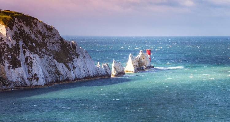 Les falaises de craie blanches spectaculaires des Needles surgissent dans la mer bleu étincelant, couronnées par un phare rouge et blanc.