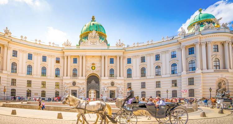 Carruaje tirado por caballos y turistas frente al complejo imperial Hofburg de Viena en un día soleado.