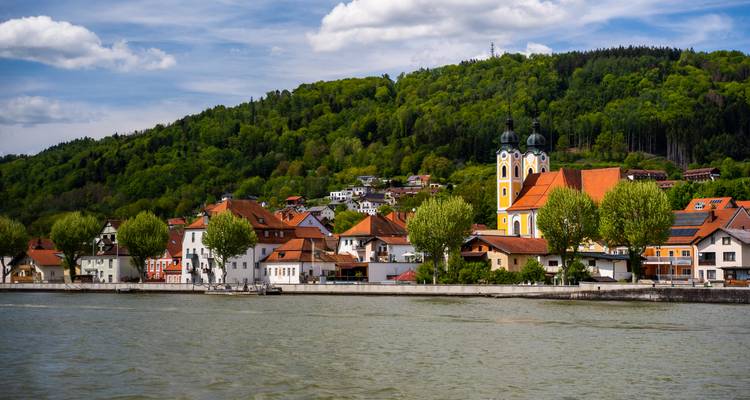 Encantador pueblo ribereño respaldado por colinas boscosas e iglesia amarilla de torres gemelas sobre el Danubio.