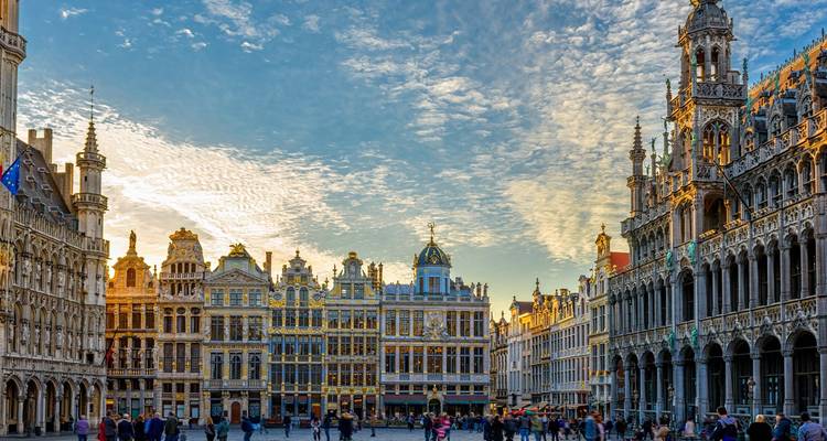 Grand Place à Bruxelles avec ses maisons de guildes ornées et la flèche imposante de l'hôtel de ville sous un ciel dramatique, des visiteurs se promenant